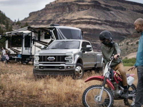2024 Ford Super Duty parked in a grassy field with an RV and boy on a dirt bike